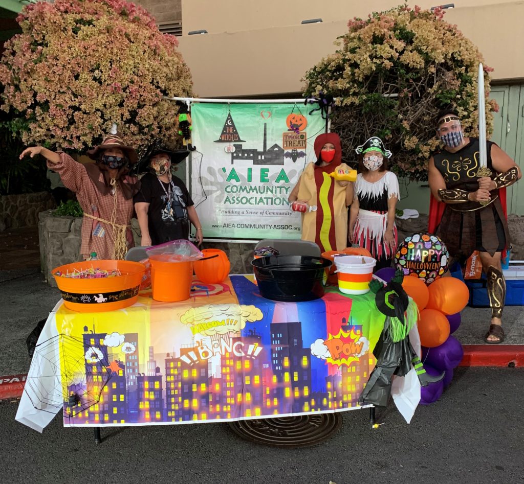 Several adults in Halloween costumes in front of an 'Aiea Community Association banner